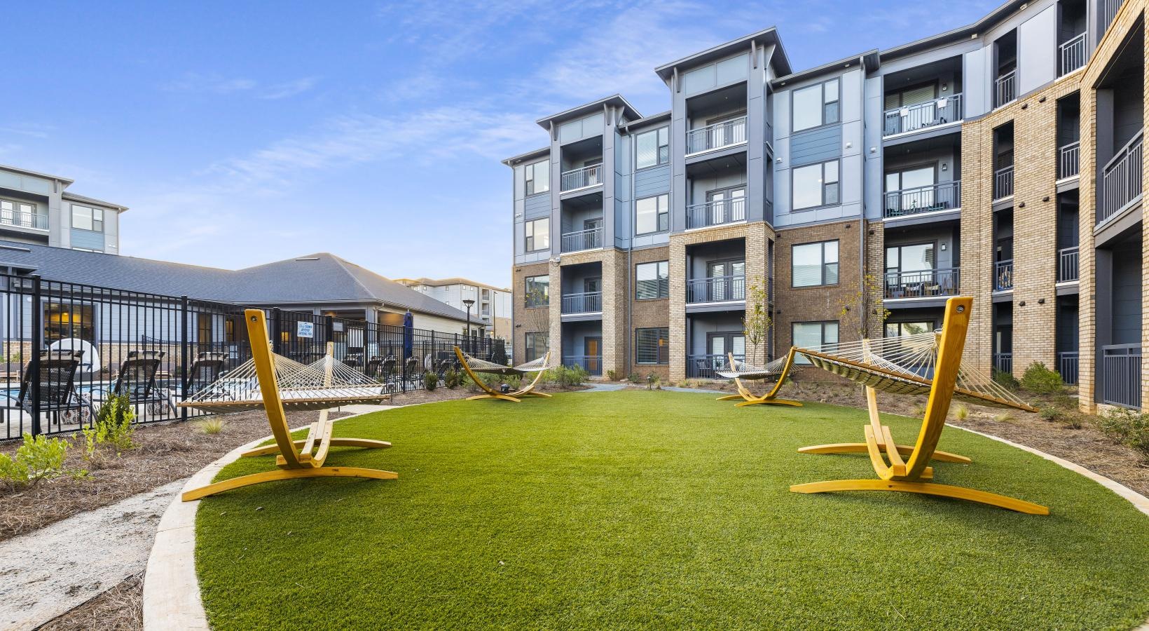 a group of hammocks on a green lawn with a building in the background