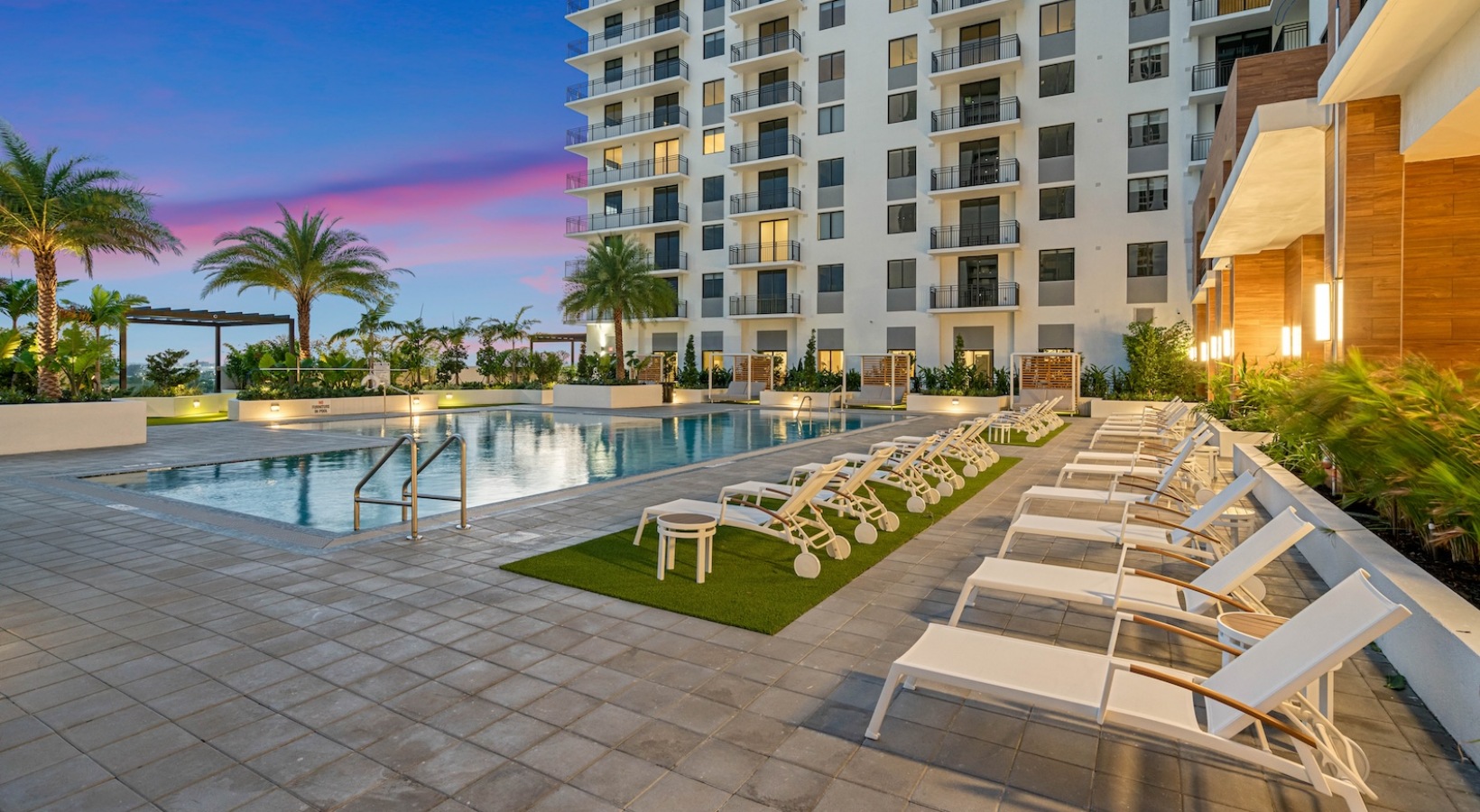 a pool with lounge chairs and palm trees in front of a building