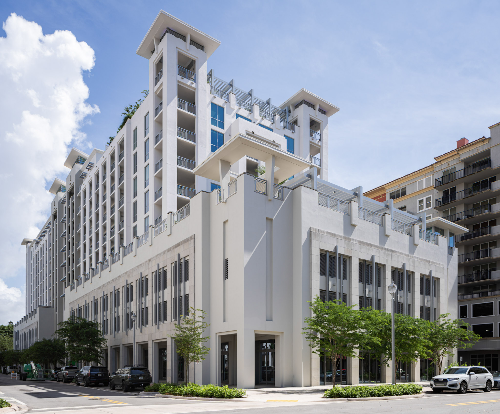 a white building with trees and cars parked on the side