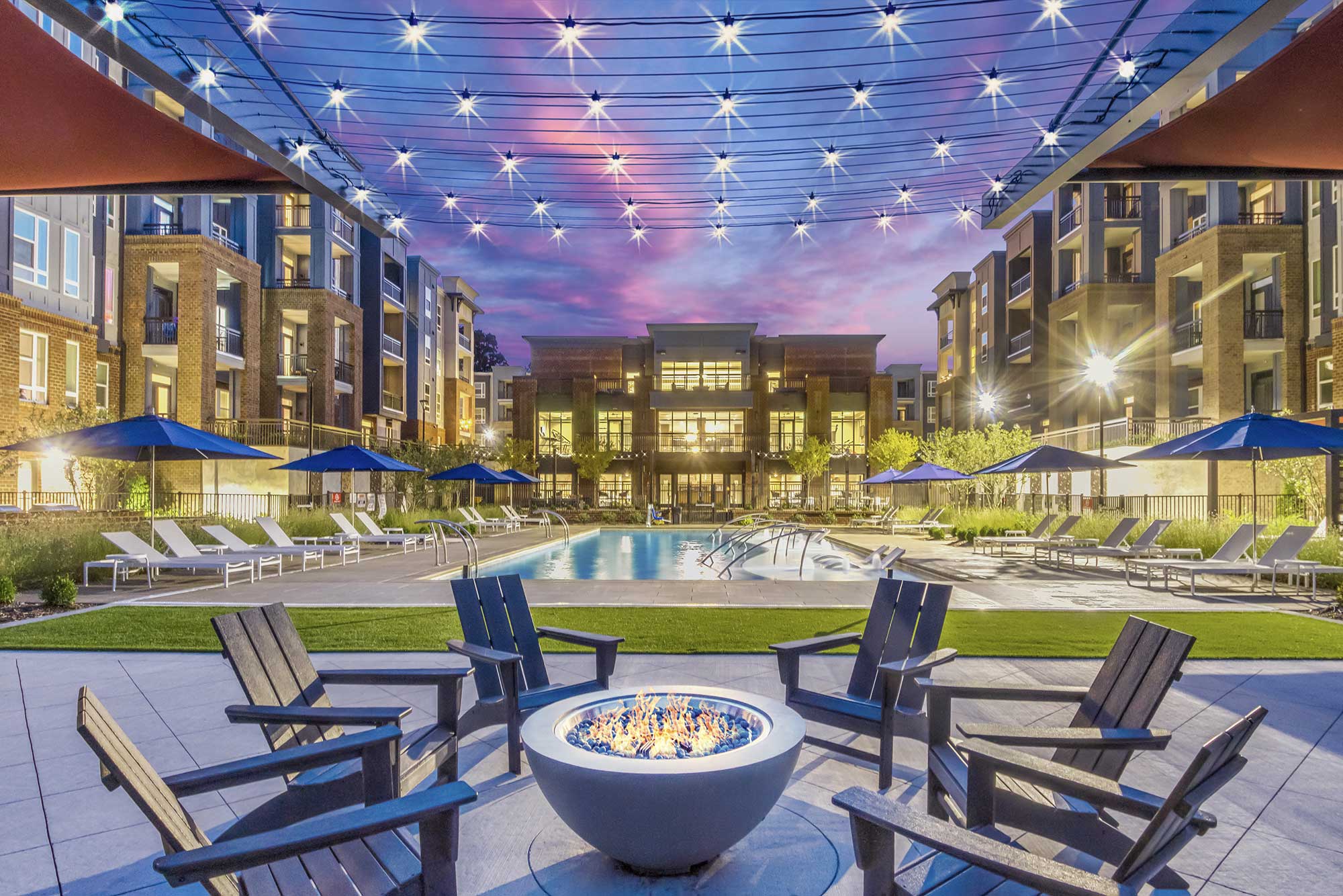 a pool with chairs and a fire pit in front of a building