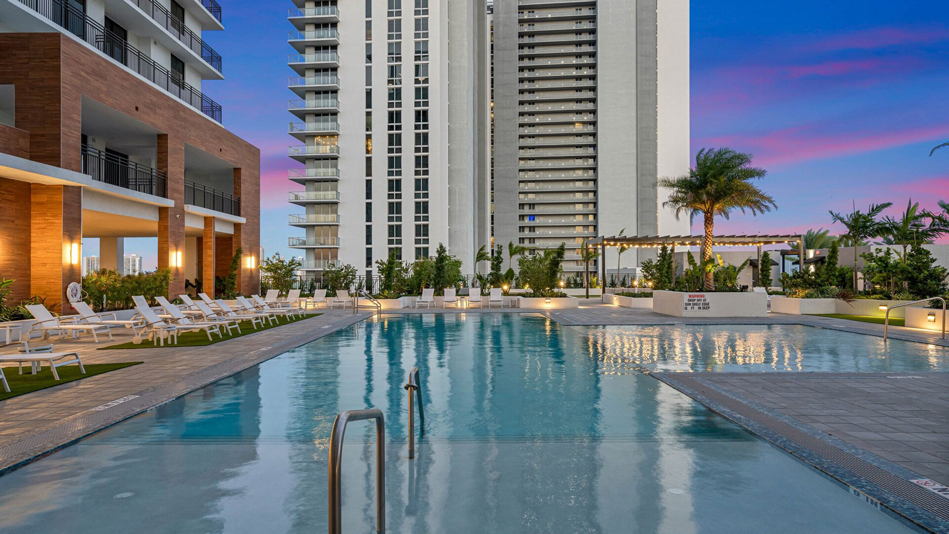 a pool with chairs and palm trees in front of buildings